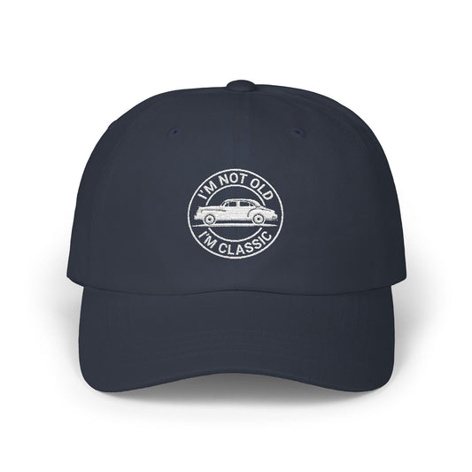 Man wearing a black hat with white embroidered vintage car design and text that reads “I’m Not Old I’m Classic” in a circular badge style