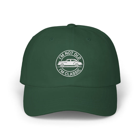 Man wearing a black hat with white embroidered vintage car design and text that reads “I’m Not Old I’m Classic” in a circular badge style