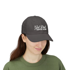 Woman wearing a black hat with mixed-script embroidered text reading “Girl Dad Super Hero” standing against a chain-link fence